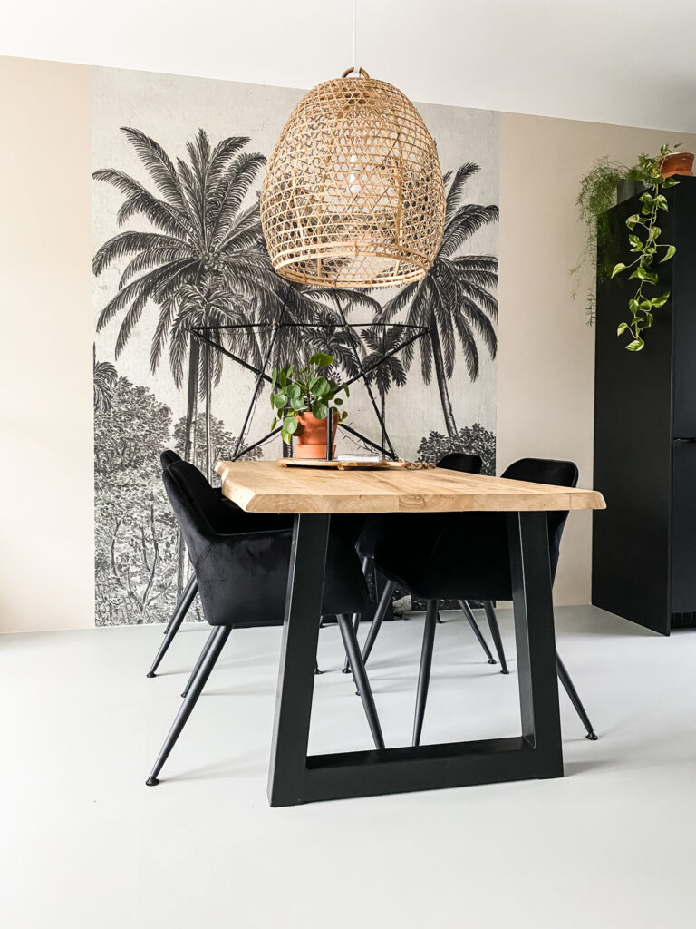 eethoek in tropische sfeer met palmbomen behang, een stoere eiken tafel met trapeze poot en zwart velvet stoelen