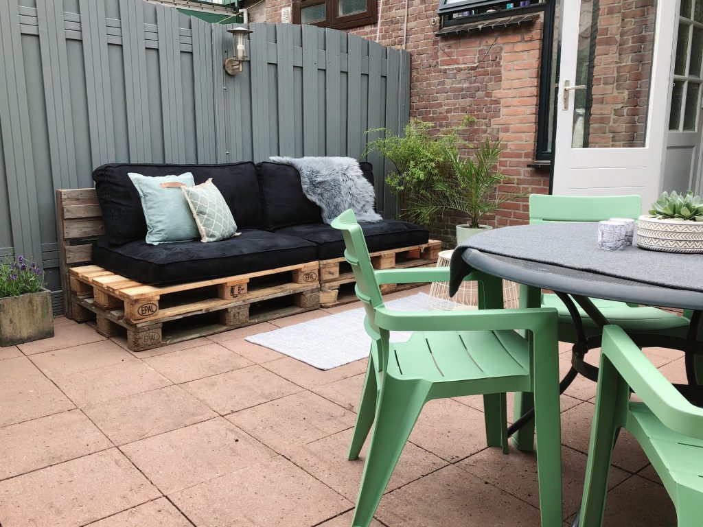 tuin make-over resultaat: groene tuinstoelen met palletbank op de achtergrond met zwarte palletkussens